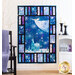 A decorative quilt hangs on a wall, featuring a central design of a serene winter scene with a church and trees, surrounded by a border of colorful geometric patterns in shades of blue, purple, and white. The setting is cozy, with a chair and candles visible nearby.