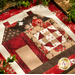 Close up of a finished quilt block depicting a house made with red and cream fabrics with decorative greenery draped around the edges.