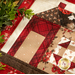 Close up of a finished quilt block depicting a house made with red and cream fabrics with decorative greenery draped around the edges.