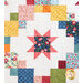 A colorful quilt featuring a patchwork design with various floral and patterned squares in shades of blue, pink, orange, yellow, and green, arranged on a light background with subtle textures.