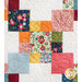 A colorful quilt featuring a patchwork design with various floral and patterned squares in shades of blue, pink, orange, yellow, and green, arranged on a light background with subtle textures.