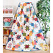 A colorful quilt is displayed draped over a wooden stand. The quilt features various star patterns and bright squares in colors like red, blue, green, and orange. In the background, there is a shelf with potted plants and decorative items.