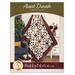 Front cover of the Aunt Dinah Throw Quilt pattern showing a finished quilt draped in front of a white paneled wall with furniture and a houseplant