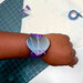 A hand wearing a purple heart-shaped slap band with a silicone band, above a green cutting mat.