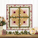 Photo of a floral wall hanging on a white paneled wall with floral decor, books, and a pink jar on a brown countertop at the bottom of the image