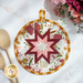 Close up photo of a round folded star hot pad made with pink, white, and red floral fabrics with yellow gingham laying flat on a white countertop with wooden spoons and a bouquet of flowers