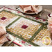 Close up photo of a table runner made with log cabin blocks and cream, yellow, green, and red floral fabrics surrounded by place settings with matching napkins