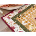 Close up photo of a table runner made with log cabin blocks and cream, yellow, green, and red floral fabrics with a place setting and matching napkin in the background just off camera