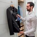 man using handheld steamer to steam a black suit jacket