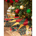 Photo of a decorated Christmas tree with an elaborate tree skirt beneath it with gold wrapped gifts in the background