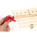 Photo of someone holding a tiny red bow in two fingers with the bow maker disassembled in the background on a white surface.