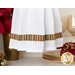 Close up photo of the bottom of a hanging towel made with metallic striped Christmas fabrics hanging on front of a white shelf containing a poinsettia, gold dishware and winter decor items