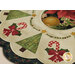 A decorated table mat featuring green Christmas trees, red bows, and candy cane motifs, with a circular design and a floral border.