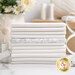 A stack of white on white fat quarters, surrounded by sewing supplies and flowers.