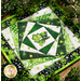 Photo of the finished wall hanging featuring offset squares in shades of green with a shamrock and top hat in the center laying flat on a table and framed by green foliage