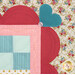 Close-up of a colorful quilt showcasing a decorative border with a heart, scallops, and button details in pink, red, and teal fabric with floral patterns.