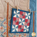 A close up shot on the mini quilt hung from twine and clothespins, demonstrating fabric and embellishment details.
