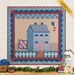 The completed Little Garden House in Summer wall hanging in a blue and red palette from the Creating Memories collection, hung on a white-paneled wall and staged with coordinating decor and leafy plants.