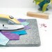 An Oliso iron rests on a gray pressing mat with colorful fabric pieces, alongside a wooden tool and pins.