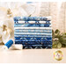 A stack of the fabrics included in the Holiday Flourish Festive Finery Blue FQ set, with trees and pointsettas and mistletoe and thread.