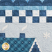 A detailed patchwork quilt featuring various shades of blue. The design includes patterned fabric sections with snowflakes, checkered patterns, and quilted motifs, along with a blue house roof near the bottom with a white snowflake nearby.