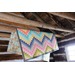 Colorful zig zag patchwork quilt draped over a wooden beam in a rustic cabin.