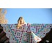 A girl peeks over a colorful patchwork quilt draped on a wooden structure