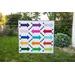 A quilt featuring colorful arrows in various directions, displayed in a grassy backyard.