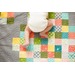 A baby in a white onesie crawls on a colorful patchwork quilt with various patterns.