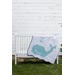 a white and blue whale quilt with a scalloped edge drapped over a crib