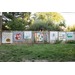 Colorful quilt patterns are displayed along a wooden fence in a grassy yard.