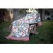 A colorful quilt draped over a wooden chair in a grassy outdoor setting.