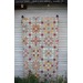 A colorful quilt with star patterns hanging on a white wooden wall, surrounded by green foliage.