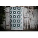 A teal quilt hanging on a weathered wooden fence, featuring intricate geometric patterns with a white background.