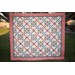 Colorful chain quilt hanging outdoors, featuring a geometric pattern with floral borders