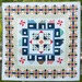 A colorful quilt featuring geometric patterns, houses, and pinwheels, framed by a multicolored border.