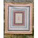 A colorful quilt with around the world patterns in concentric rectangles displayed against a stone wall.