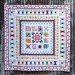 Colorful quilt with house blocks and intricate patterns and borders displayed against a rustic wooden background.