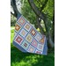 A colorful quilt with around the world blocks draped over a tree branch, set against a green lawn and sunny sky.