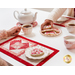 Two people enjoying tea and cookies on the placemats; just their arms are visible, holding a teacup and reaching for a cookie.