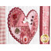 Close up photo of a pink, red, and white wall hanging featuring one of the four hearts covered in charms, buttons, and ribbons.