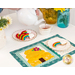 A model pours pink tea from a white teapot into a white teacup. The August placemat serves as the foreground while the plate of matching cookies sits next to the teacup and mat.