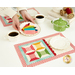 A model sets down a plate of coordinating cookies on the table next to full cups of tea. The September placemat serves as the foreground while the plate of matching cookies sits next to the teacup and mat.