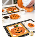 A model pours tea into a teacup next to a plate of frosted jack-o-lantern cookies in the middle of a staged table with two completed October mats in orange, black, and white.