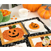 One of the October placemats with the corner of the other peeking into the bottom right side of the frame, colored in orange, black, and white, staged with a plate with an iced pumpkin cookie and a small bowl of candy corn.