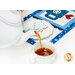 A model pours tea from a white teapot into a white teacup. The January placemat serves as the background while the plate of matching cookies peeks into frame behind the teapot.