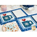 A shot of the two placemats slightly overlapping on a table set with coordinating decor. A plate of snowflake cookies rests next to the mats.