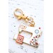 A decorative keychain shaped like a sewing machine, embellished with colorful flowers and a red design.