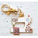 Gold keychain featuring a colorful, decorative enamel sewing machine with floral designs and a quilted square.