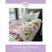 A colorful quilt titled Scrap Happy Sampler on a bed with white pillows, featuring various patterns.